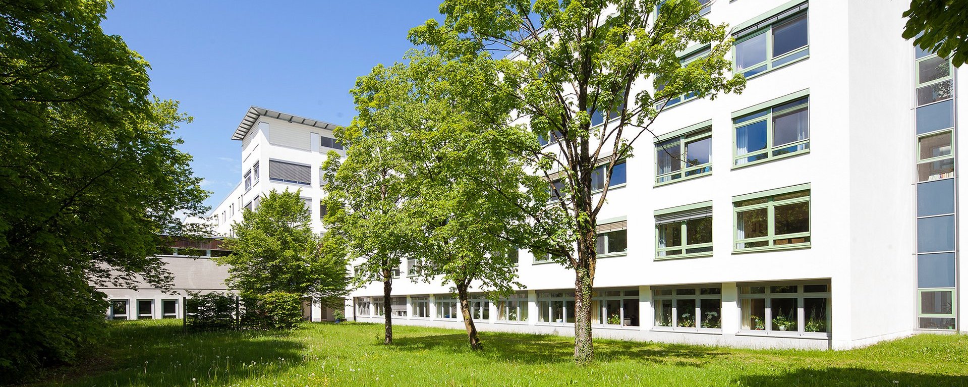 Der Garten vor den Wertachkliniken mit grünen Bäumen bei strahlend blauem Himmel