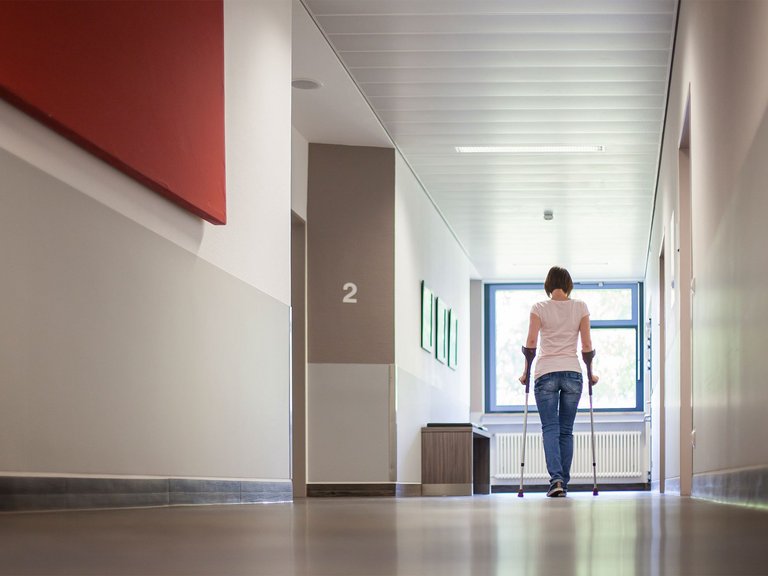 Eine Patientin läuft mit Krücken den Gang der Praxen innerhalb der Wertachkliniken entlang