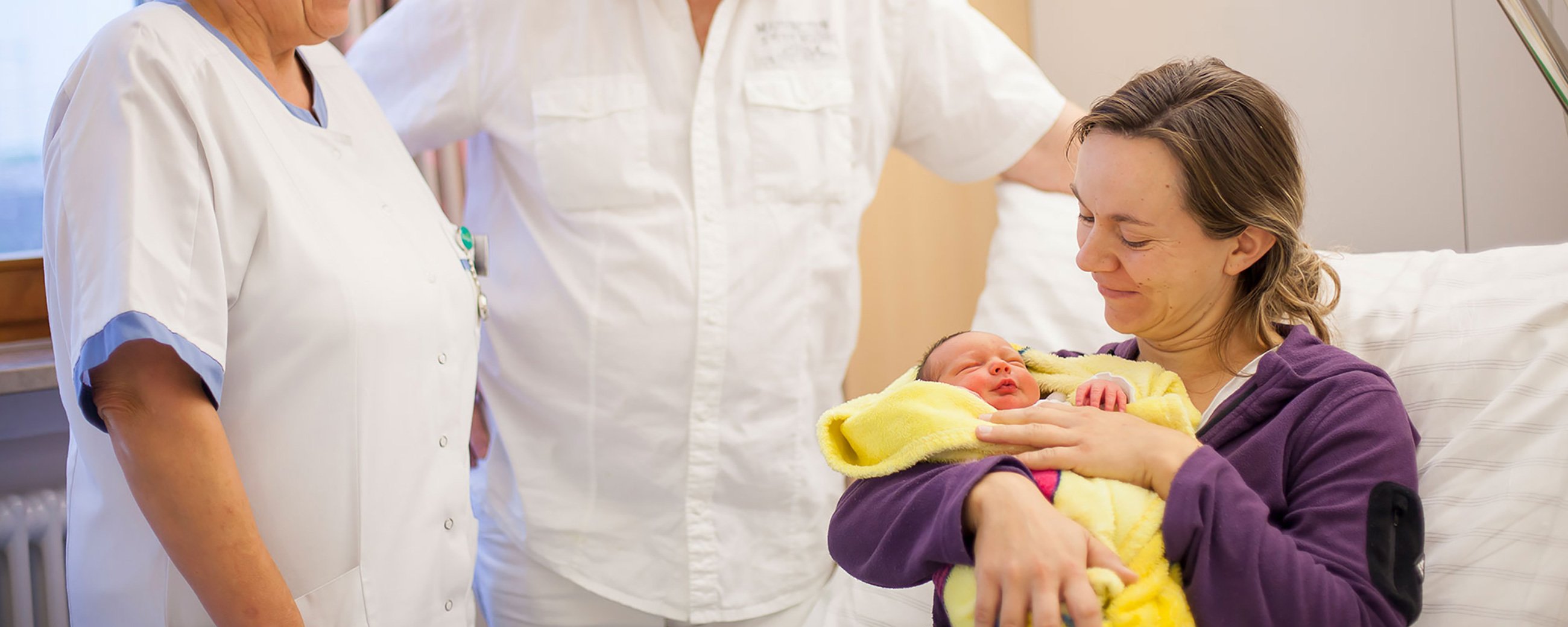 Zwei Ärzte reden mit einer Frau, die im Patientenbett sitzt und ihr neugeborenes Baby im Arm hält