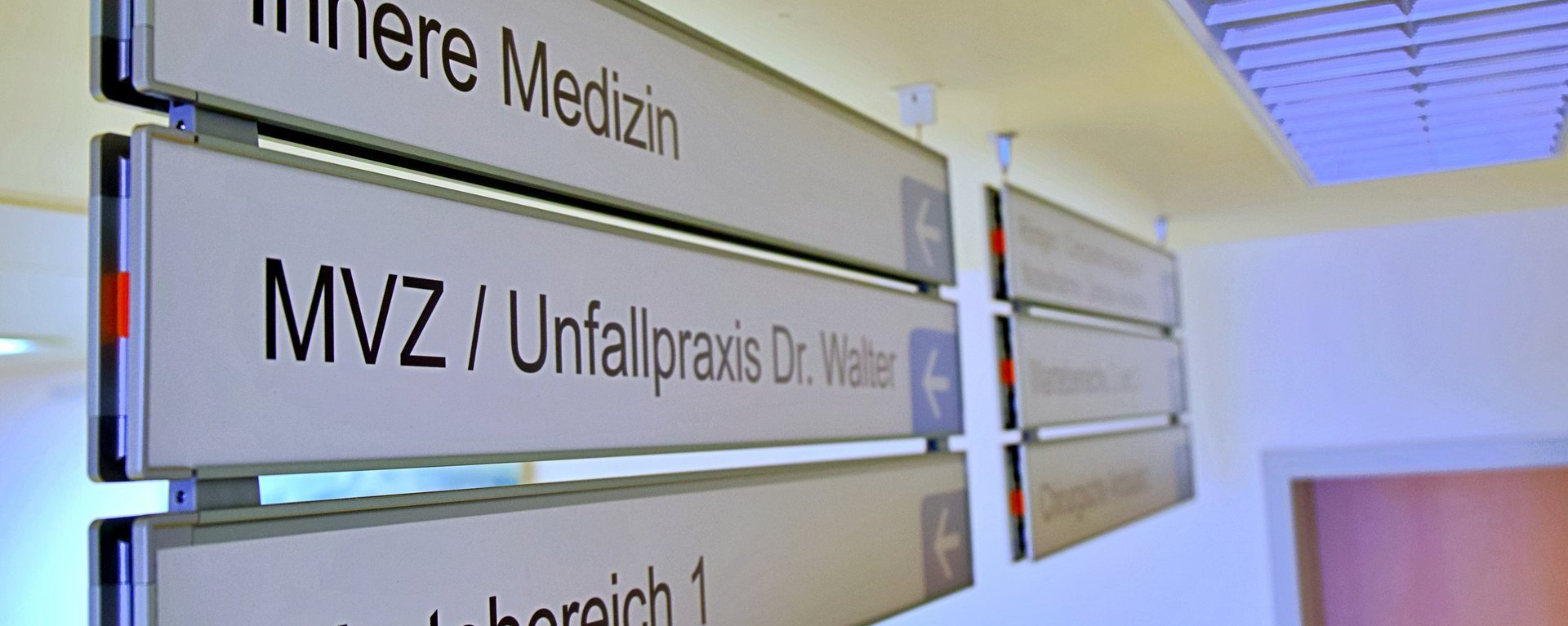 Wegweiseschilder im MVZ. Auf dem Bild sind drei Schilder mit folgenden Aufschriften zu sehen: "Innere Medizin", "MVZ/Unfallpraxis Dr. Walter" und "Wartebereich 1"