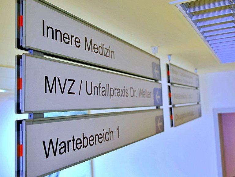 Wegweiseschilder im MVZ. Auf dem Bild sind drei Schilder mit folgenden Aufschriften zu sehen: "Innere Medizin", "MVZ/Unfallpraxis Dr. Walter" und "Wartebereich 1"