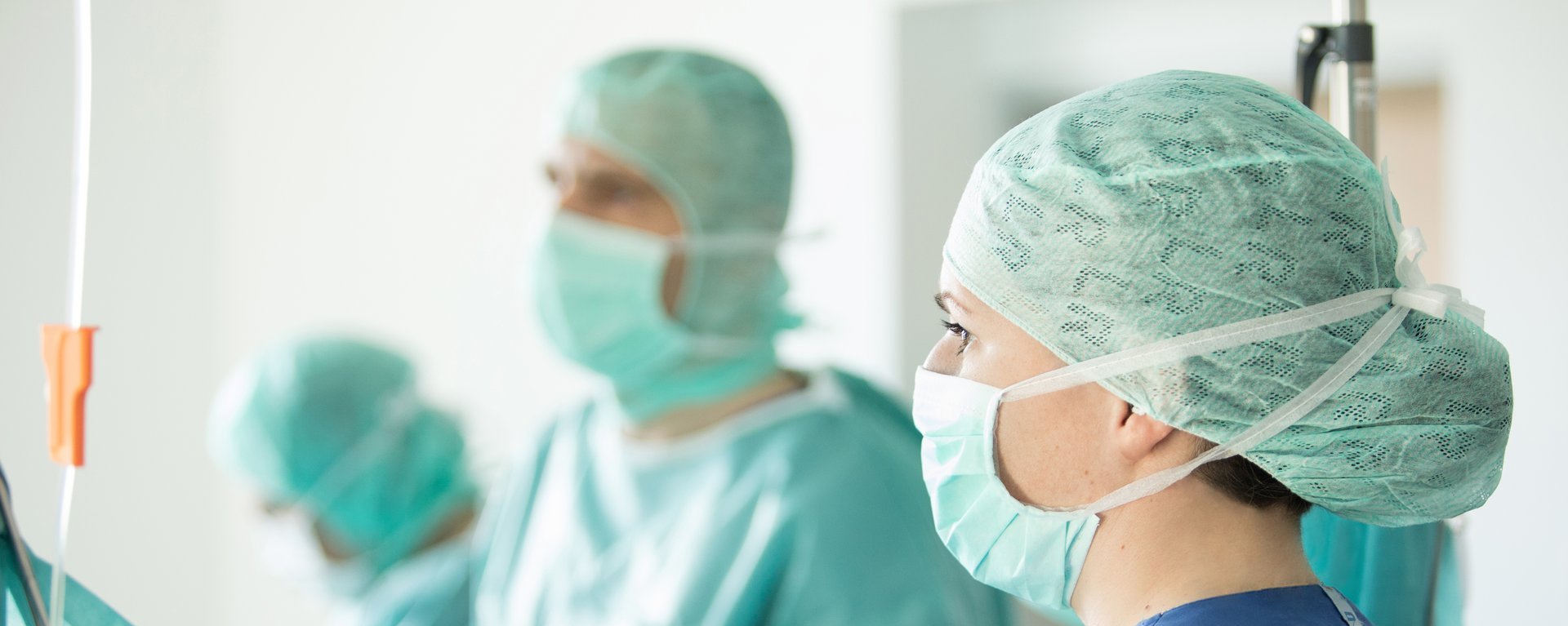 Drei Fachärzte bei einem chirurgischen Eingriff. Im Vordergrund steht eine Fachärztin mit Haarnetz und Mund-/Nasenschutz.