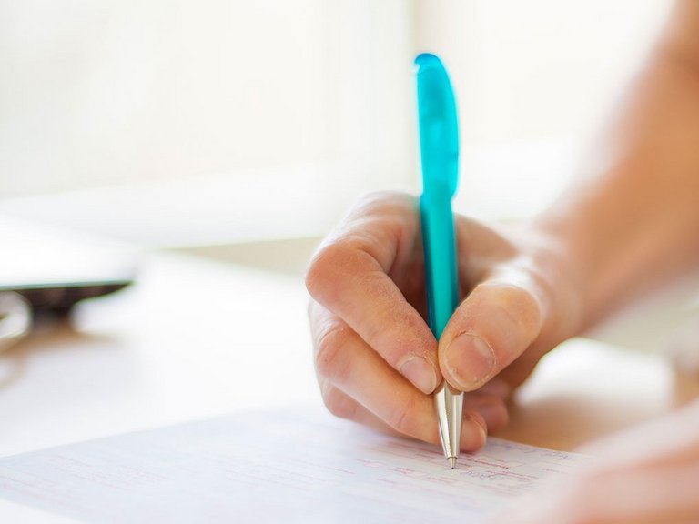 Ein Rezept wird handschriftlich mit einem Kugelschreiber von einer Person unterschrieben